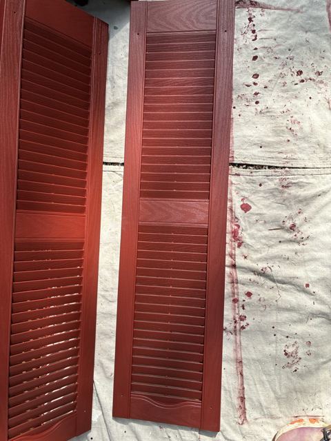 Burgundy shutters laid out on a drop cloth after painting